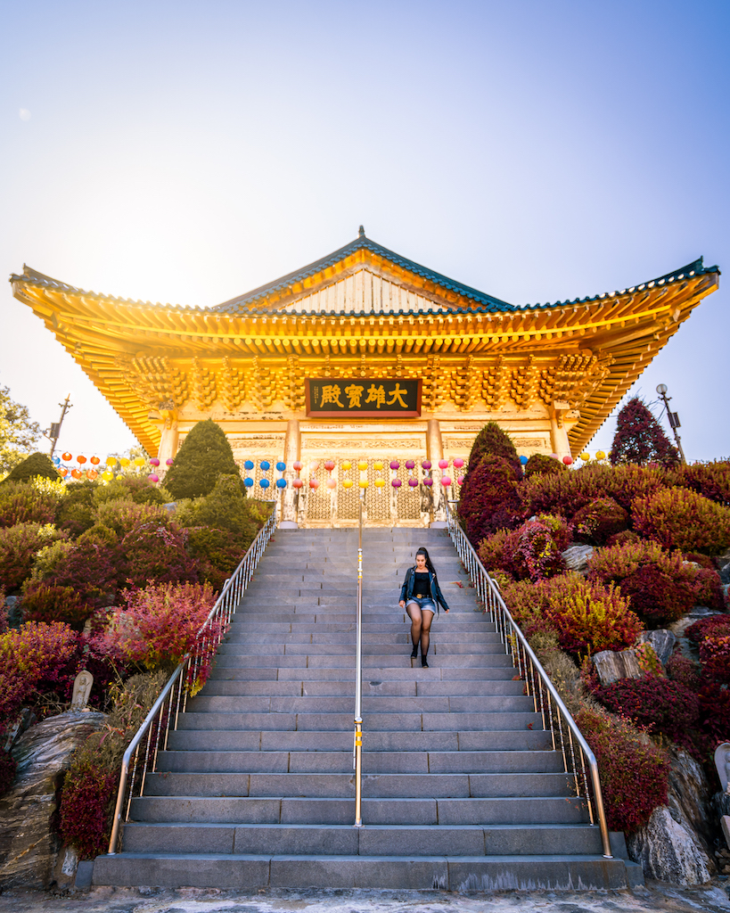 Woman standing on stone steps below Suguksa Temple's golden Buddhist hall and colorful lanterns
