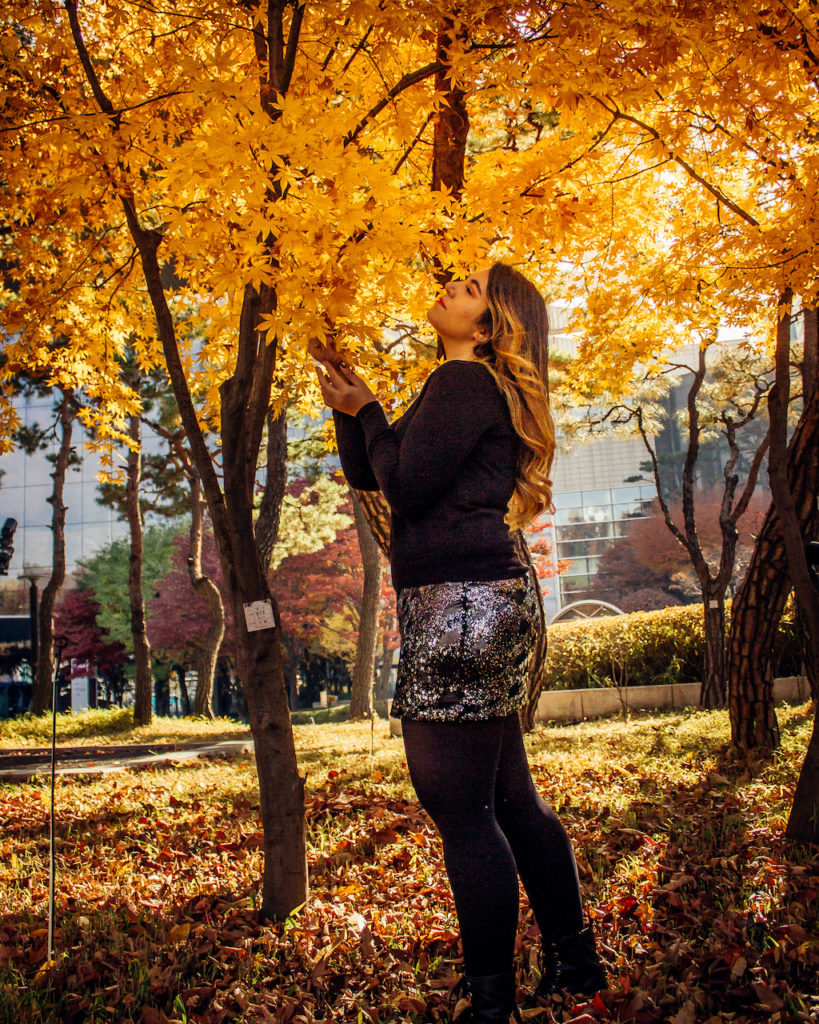 Woman posing beneath brilliant orange maple leaves at Bongeunsa Temple in Seoul