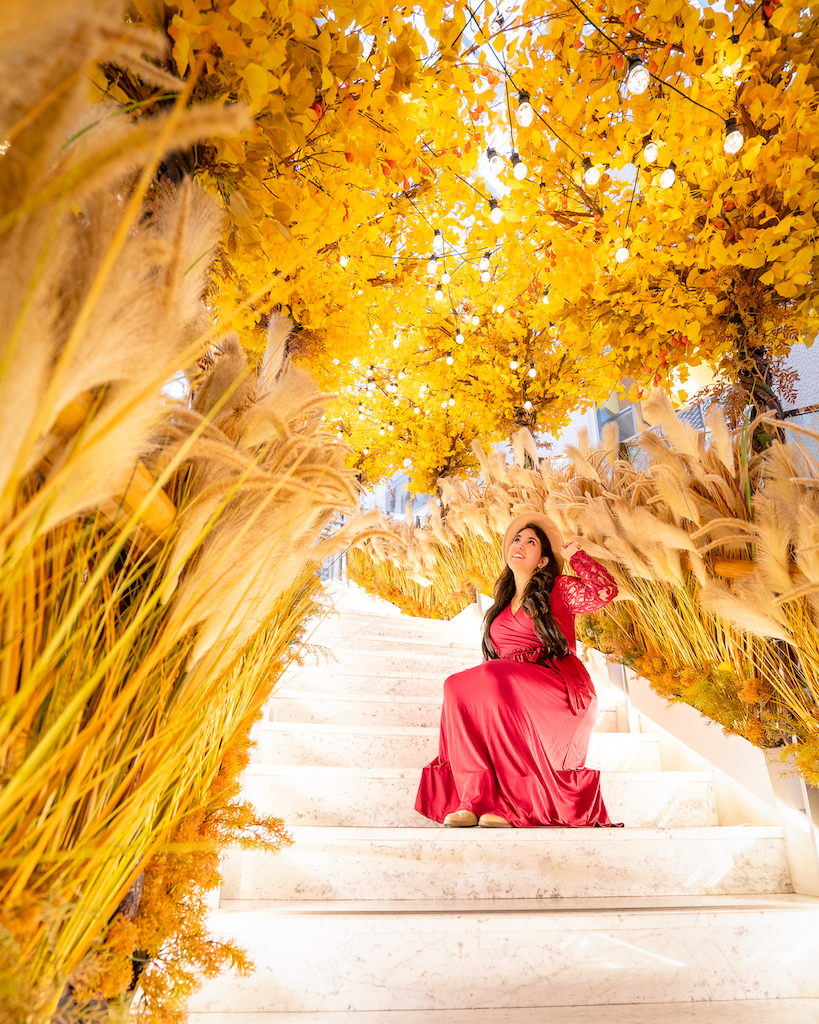 Woman in a red dress sitting on white stairs decorated with golden leaves and pampas grass at Lotte World Mall
