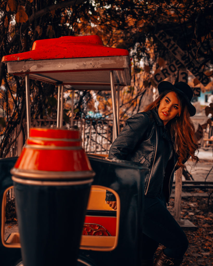 Woman in a black hat and leather jacket posing beside a vintage amusement park ride at Yongma Land